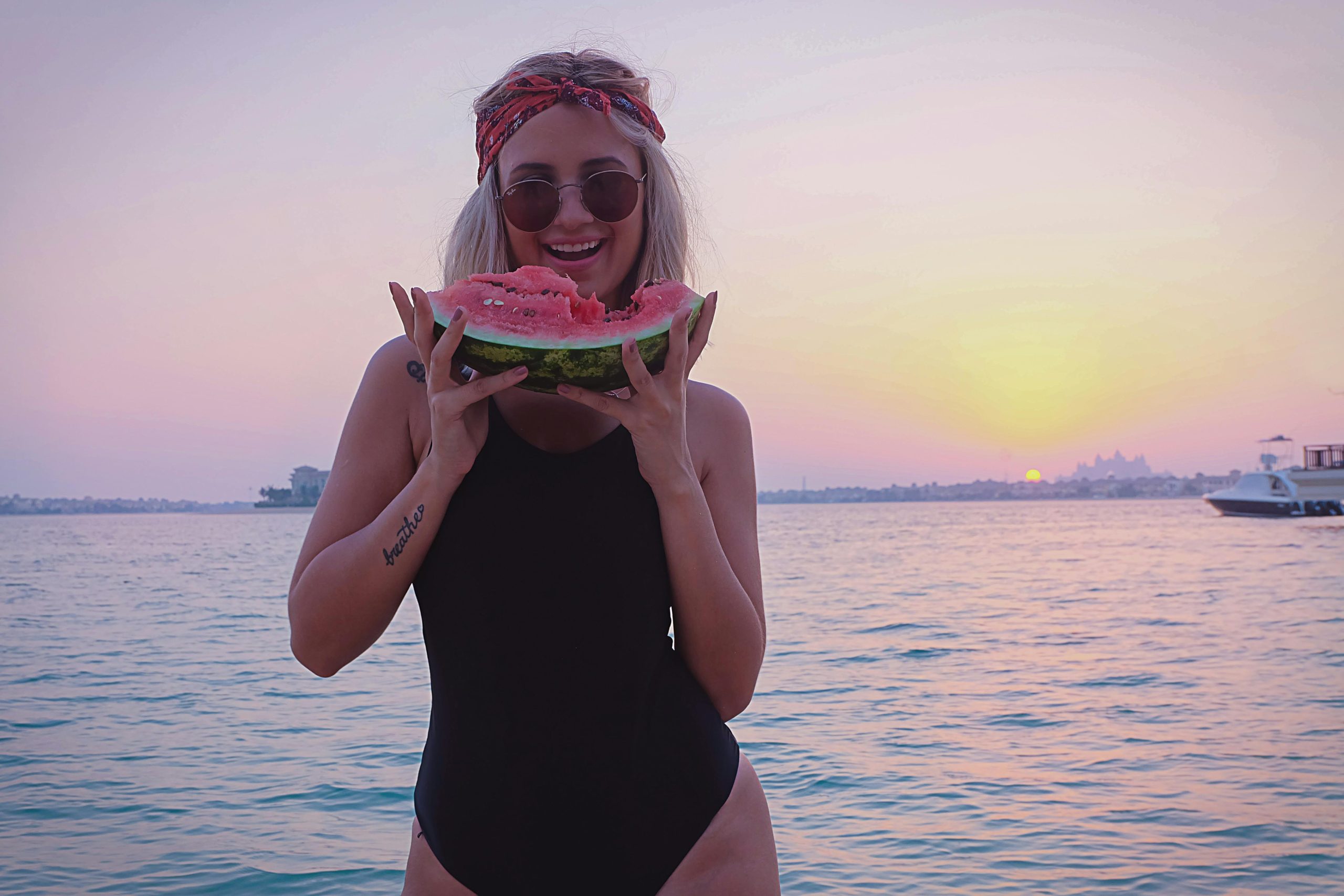A woman in a bikini enjoys a slice of watermelon by the beach during a picturesque Dubai sunset.