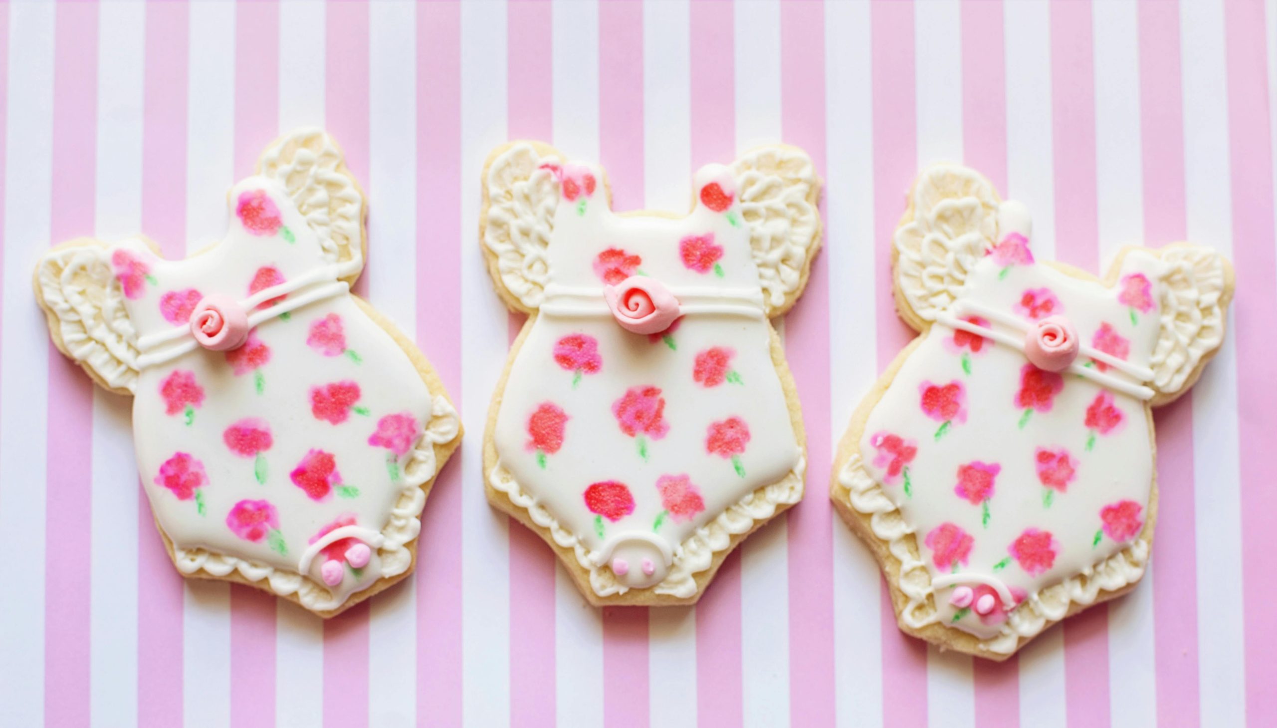 Delicately decorated baby shower cookies with floral icing on a pink striped backdrop.