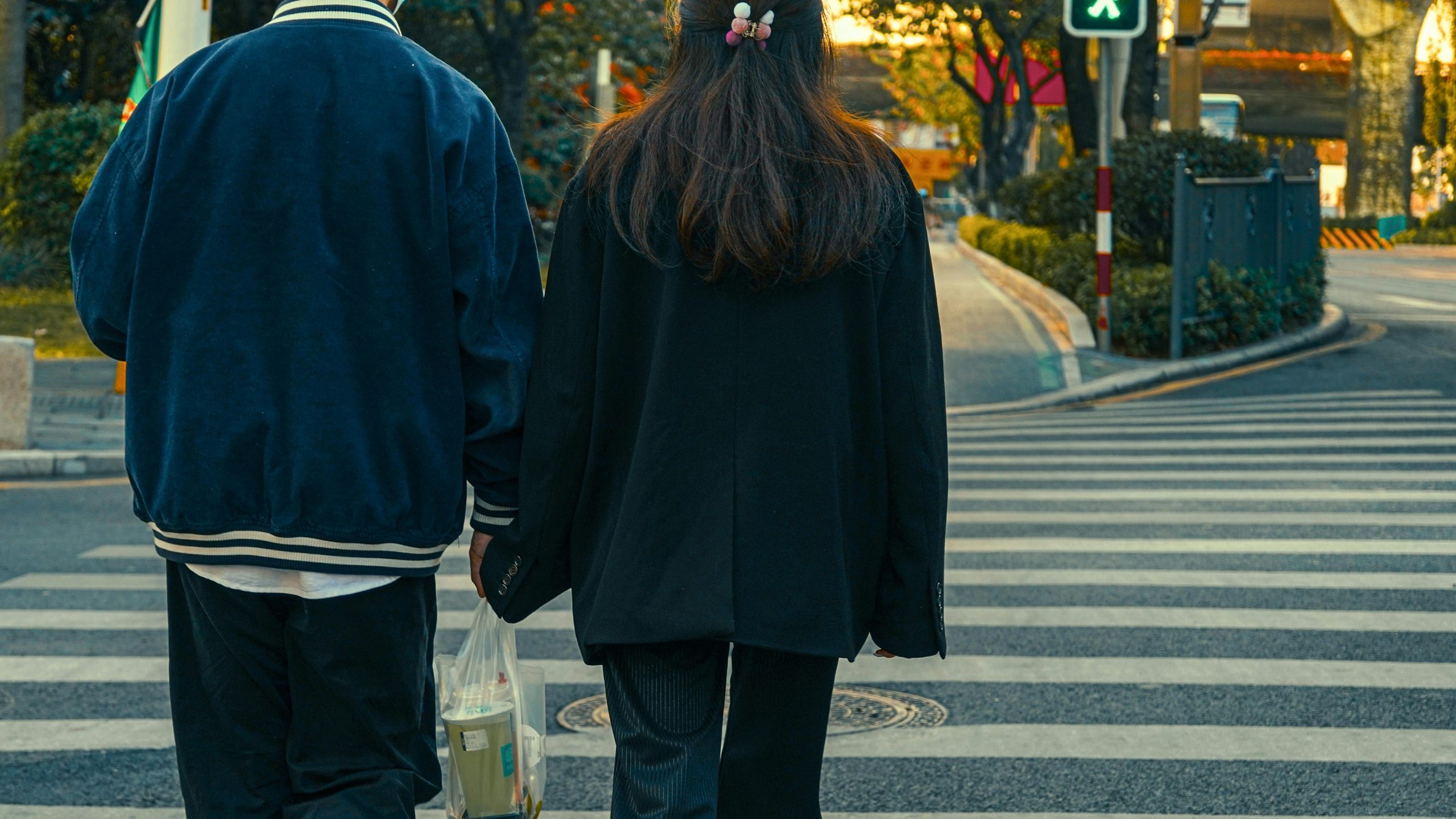 A couple holds hands crossing a pedestrian lane in an urban area during the day.