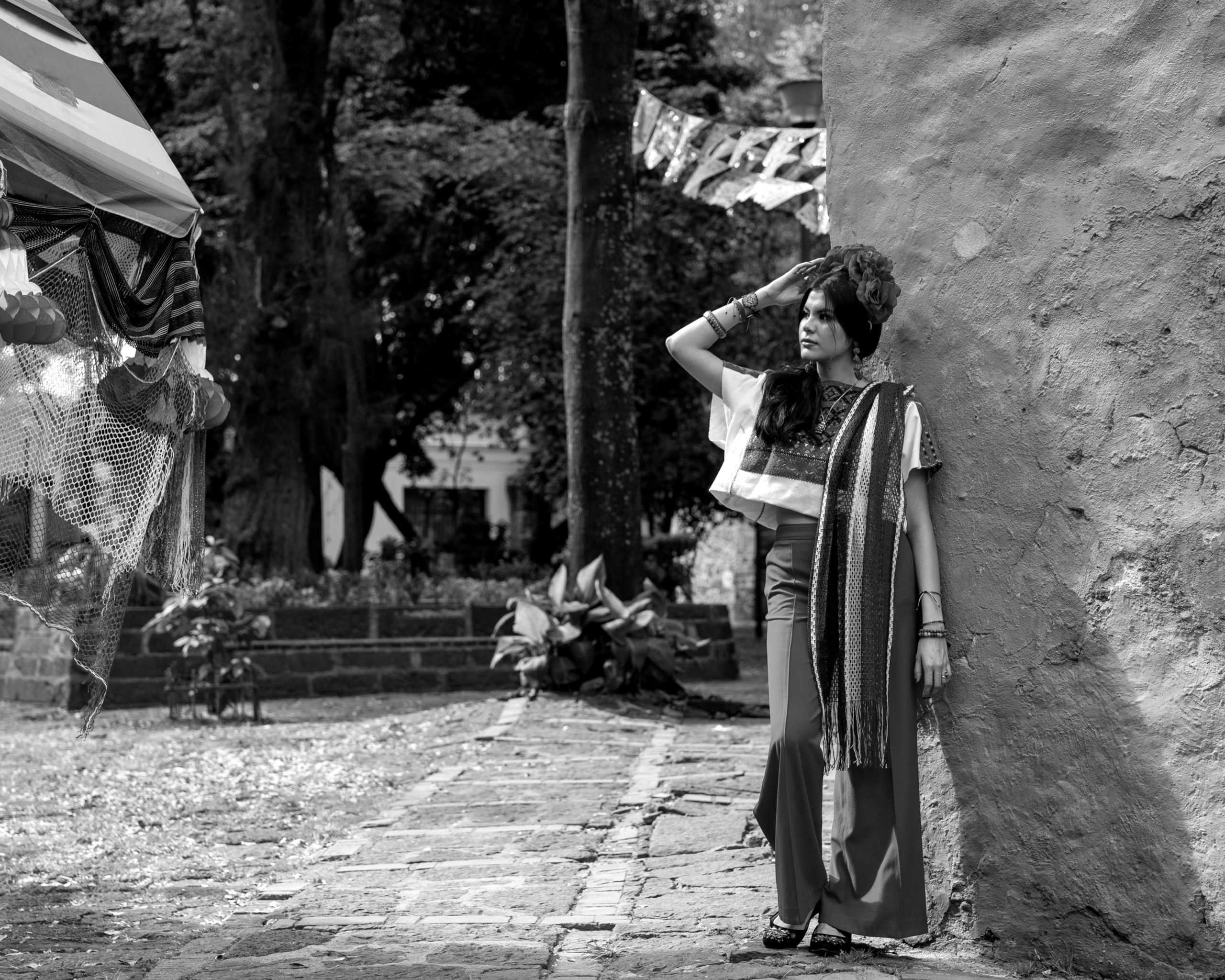 A woman in traditional Mexican clothing poses outdoors in a vibrant street scene.