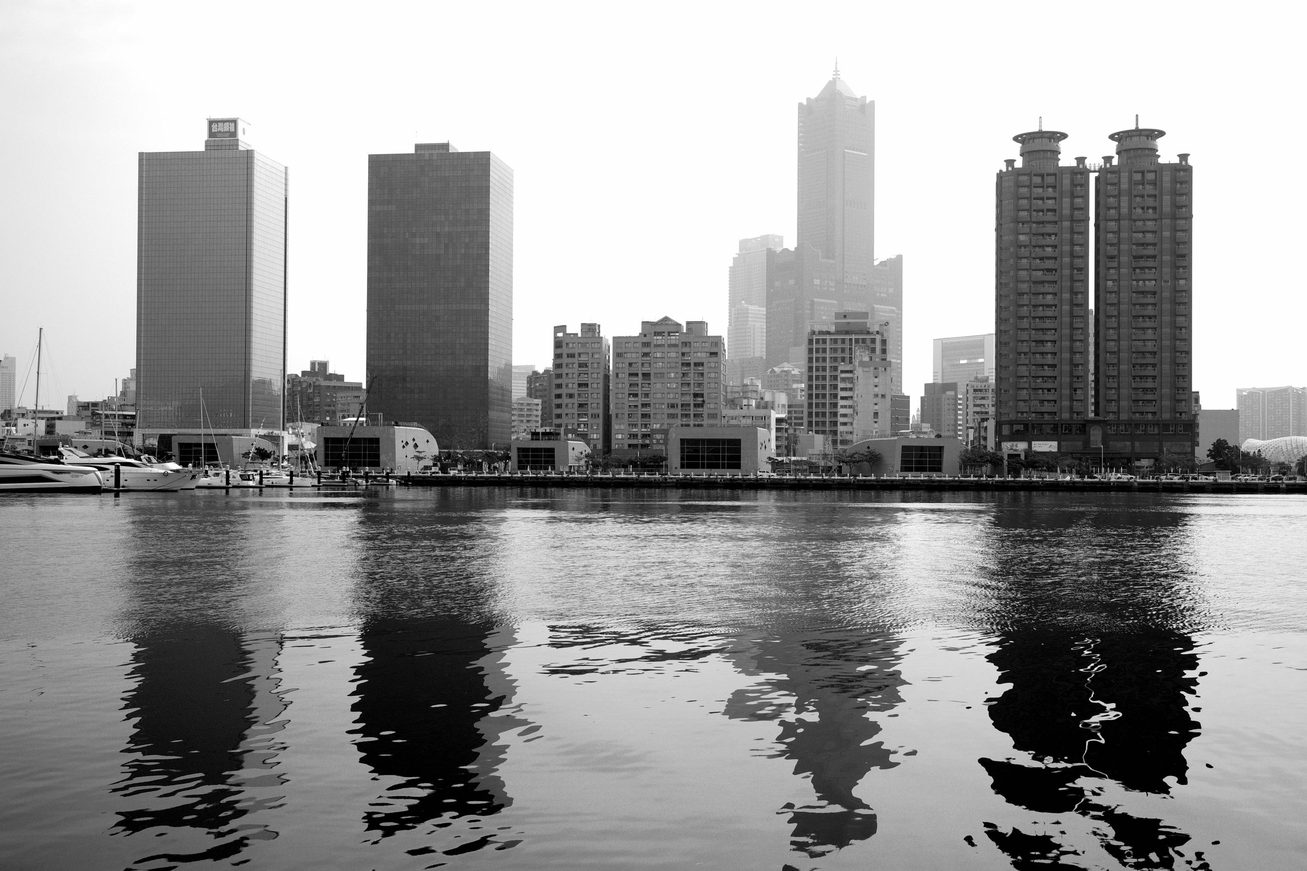 Black and white cityscape of Kaohsiung skyline with reflections on the water.