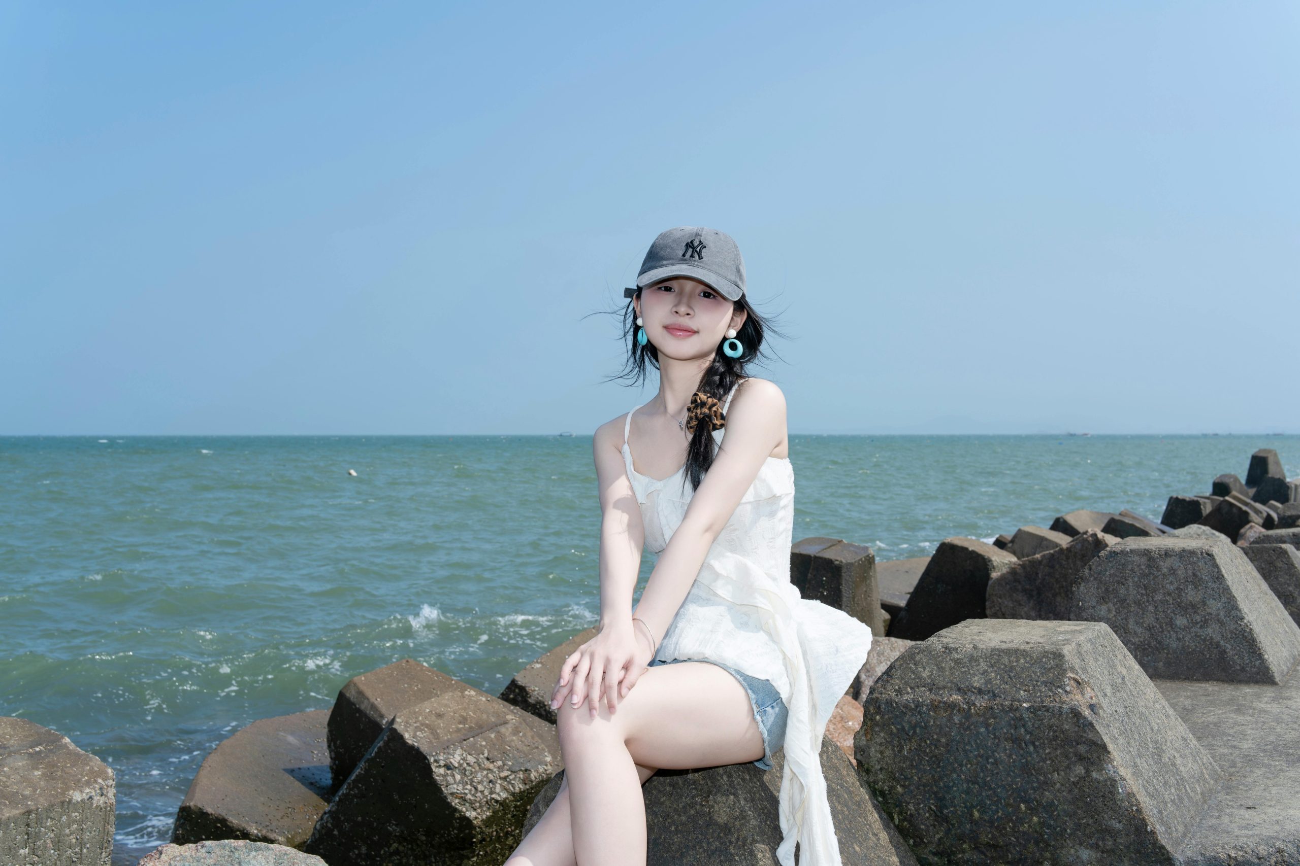 Young woman sitting on rocky seaside, enjoying a sunny day by the ocean with a calm and serene atmosphere.