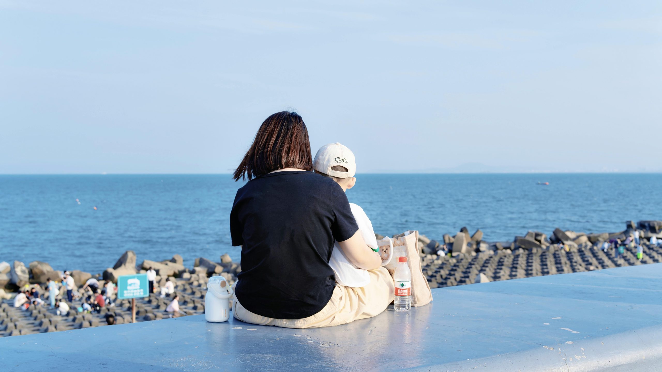 Mother and child sitting on seawall enjoying the ocean view.
