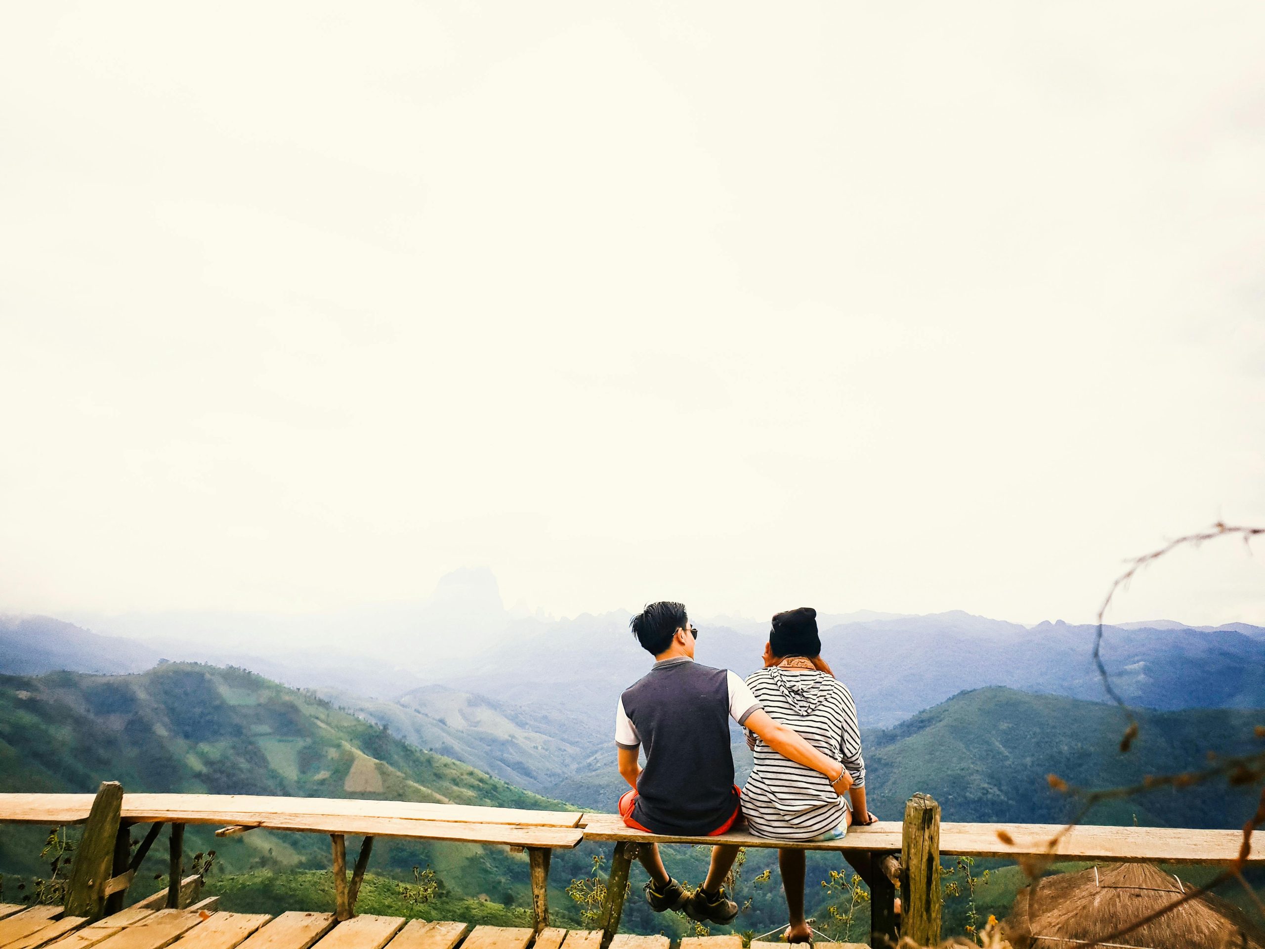 A couple sits on a bench, embracing while overlooking misty mountains in Laos.